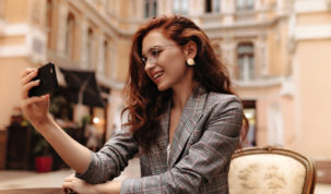 Red haired lady in grey jacket takes selfie in street cafe